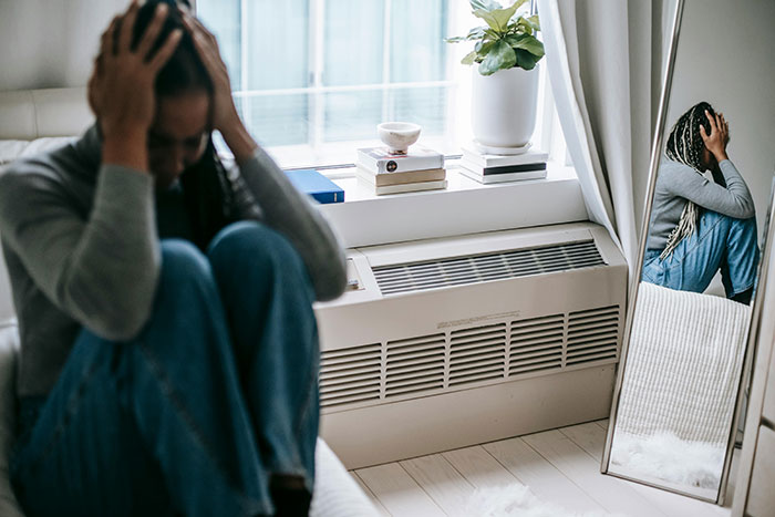 Upset woman sitting by a mirror in a bedroom, contemplating relocation to India.