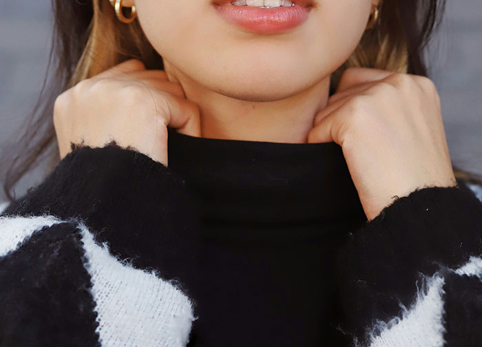 Woman wearing a black sweater, pulling the collar up, possibly hiding a mark on her neck.