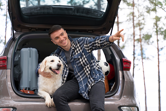 Man with dog in car trunk, smiling and pointing, outdoors.