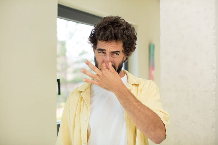 Man in yellow shirt pinching nose, illustrating questioning of hygiene. Man in yellow shirt pinching nose, illustrating questioning of hygiene.