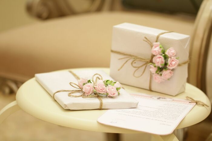 Wedding gifts wrapped in paper with pink rose decorations and twine, placed on a round table, evoking an elegant bridal theme.