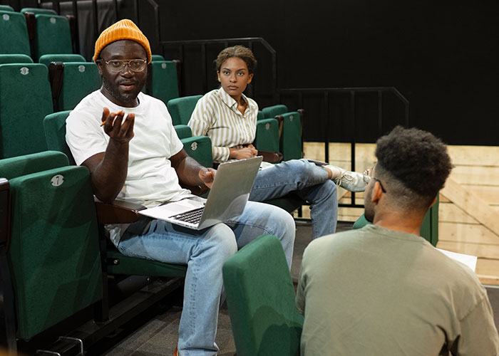 Person with laptop discussing wild audition stories with group in theater seats.