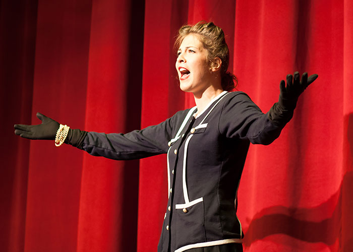 Actor passionately performing on stage in an audition, wearing a dark outfit with a red curtain backdrop.