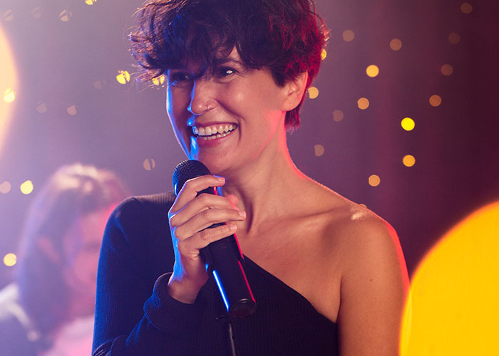 Person smiling while holding a microphone, possibly during a wild audition performance.