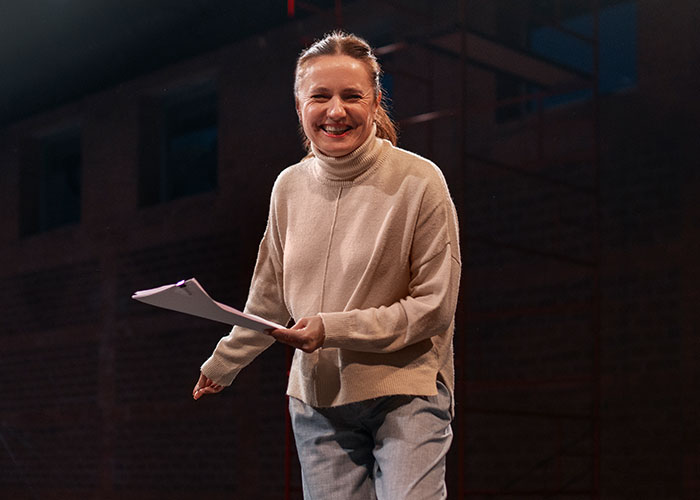 Person smiling during a theater audition, holding a script, dressed in casual attire.