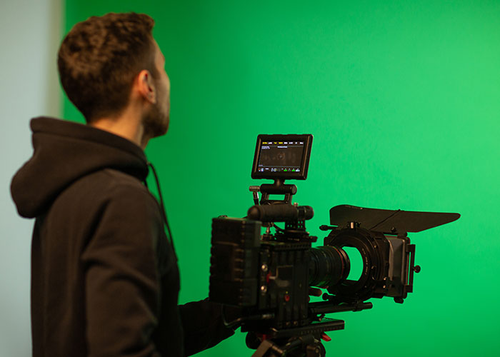 Person operating a professional camera against a green screen, capturing audition scenes.