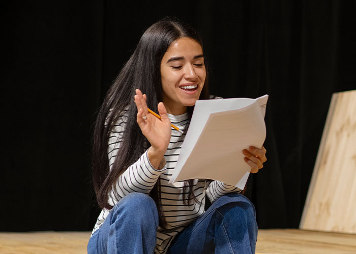 A woman in a striped shirt joyfully reads a script, illustrating a wild audition story moment.