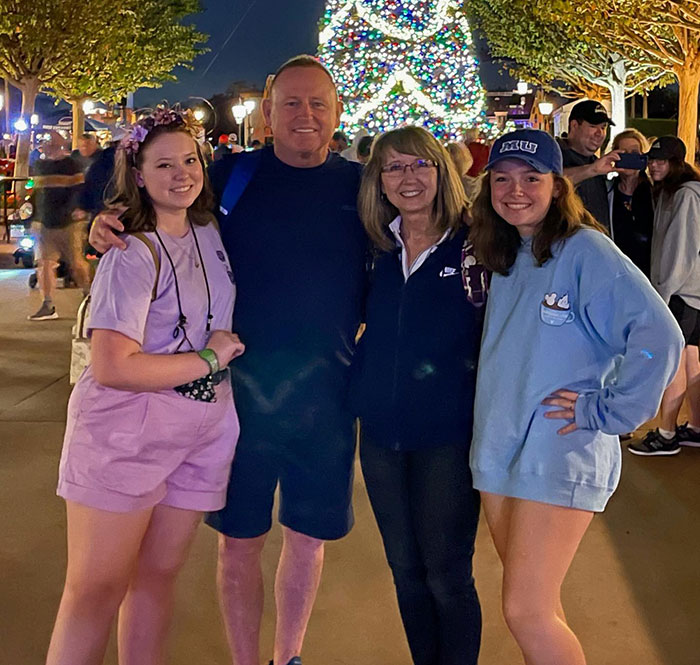 Astronaut's daughter with family, smiling by a lit Christmas tree at night, highlighting concerns for health.