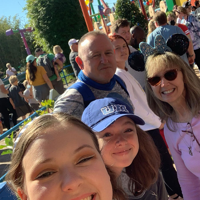 Astronaut's daughter with family at an amusement park, smiling under sunny skies.