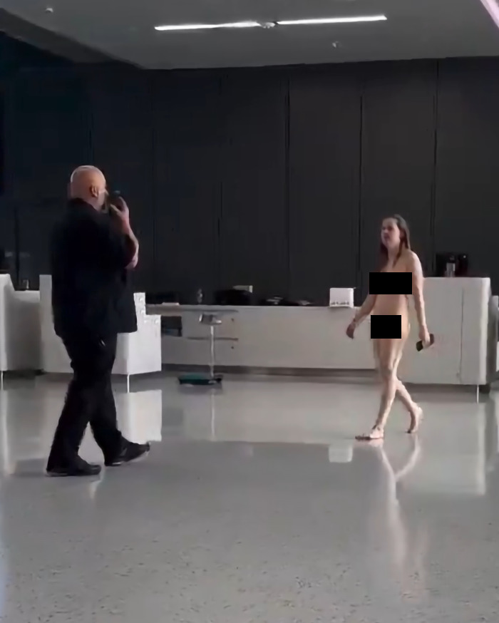 A woman having a meltdown runs unclothed through an airport, a man is nearby documenting the scene.