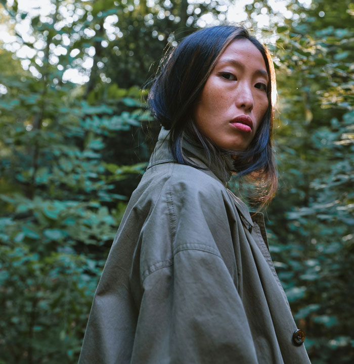 A woman in a green coat looking over her shoulder in a forest setting, related to child services inquiry.