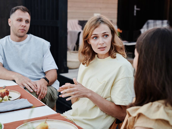 Three people having a serious conversation at a table outdoors, focusing on family dynamics and relationships. Three people having a serious conversation at a table outdoors, focusing on family dynamics and relationships.