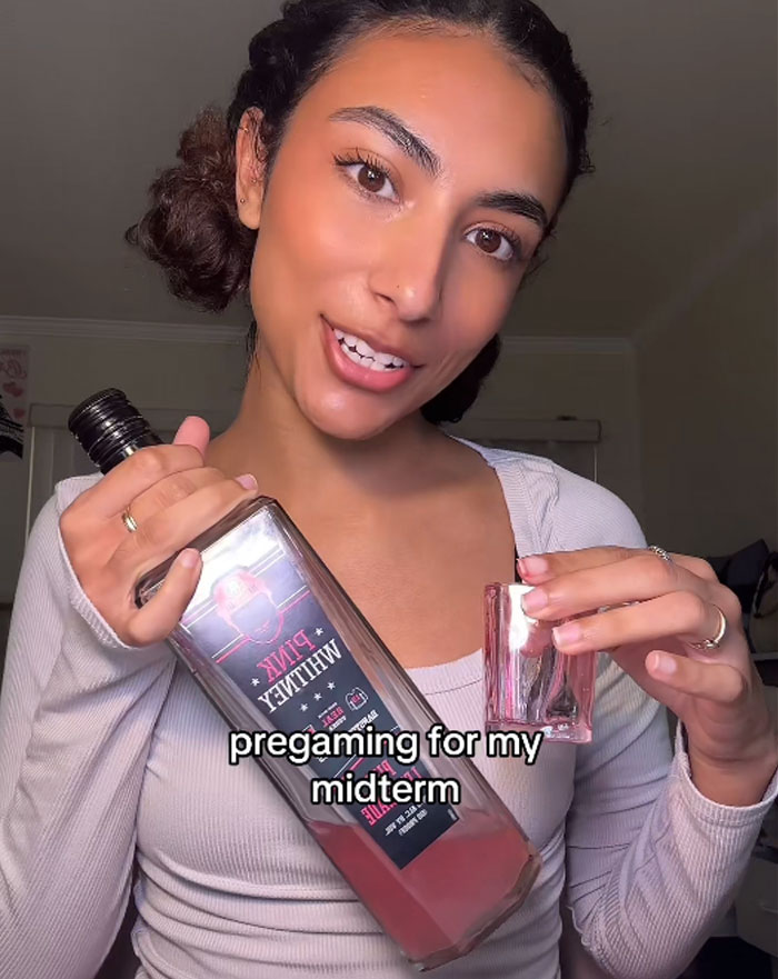 College student pregaming with a bottle, smiling, holding a glass, possibly preparing for a midterm.