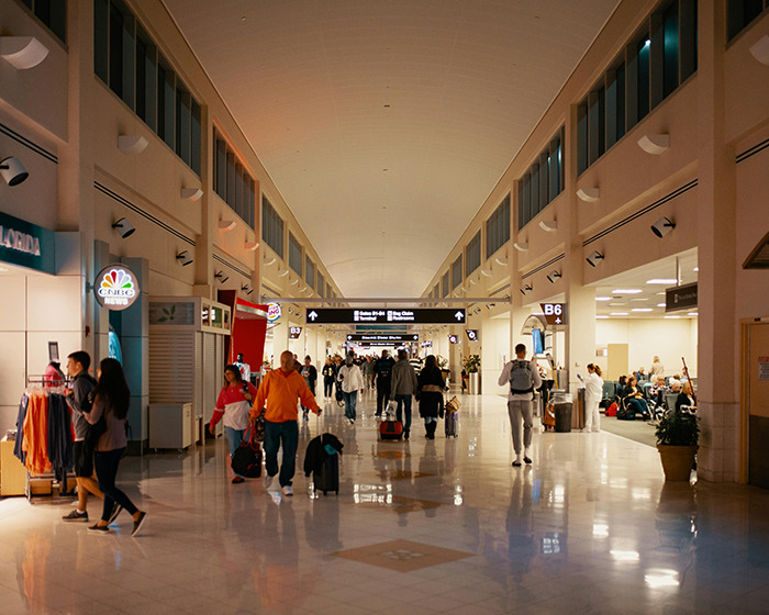 People walking through a busy airport terminal with shops and signs visible.