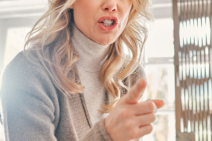 Upset woman in a sweater gesturing, light streaming through a window, possibly discussing wedding menu changes for a vegan.