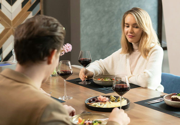 A woman and man dining together with wine, discussing relationships.