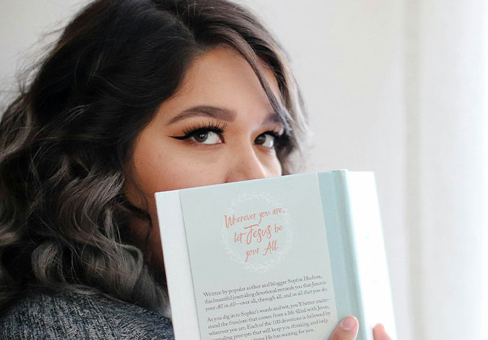Woman peeking over a book, hinting at a secret related to her neighbor's husband.