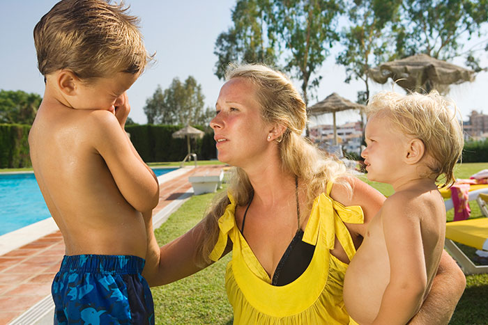 Woman at a public pool with two children, one appears upset. Woman at a public pool with two children, one appears upset.