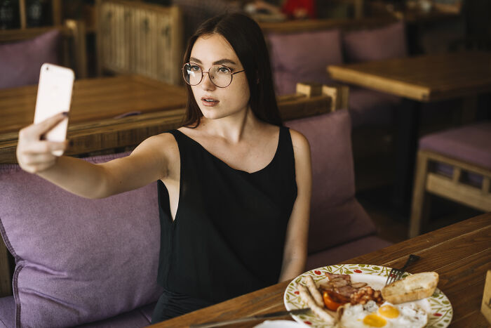 Woman in glasses taking a selfie in a cafe, breakfast on the table; focus on "never date again."