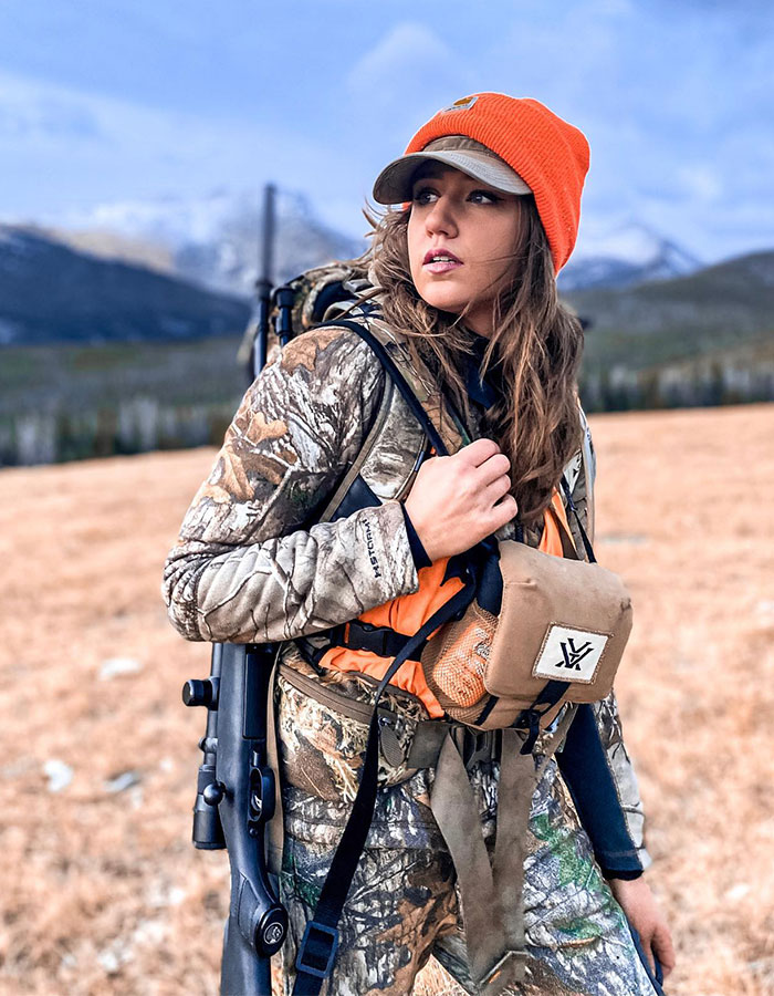 Woman in camouflage gear and orange beanie in a field, reflecting exploration. Woman in camouflage gear and orange beanie in a field, reflecting exploration.