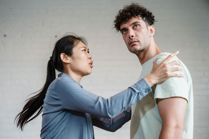 Woman demands money from her brother, gesturing urgently, indoors.