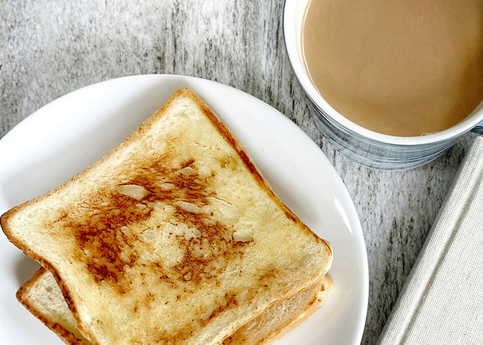 Two slices of toasted bread on a plate next to a cup of coffee, representing a simple diet meal.