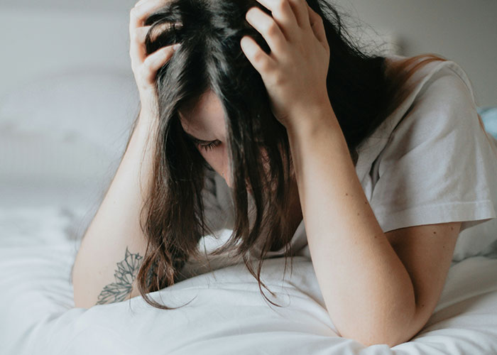 A person sitting on a bed looking distressed, possibly due to a diet.
