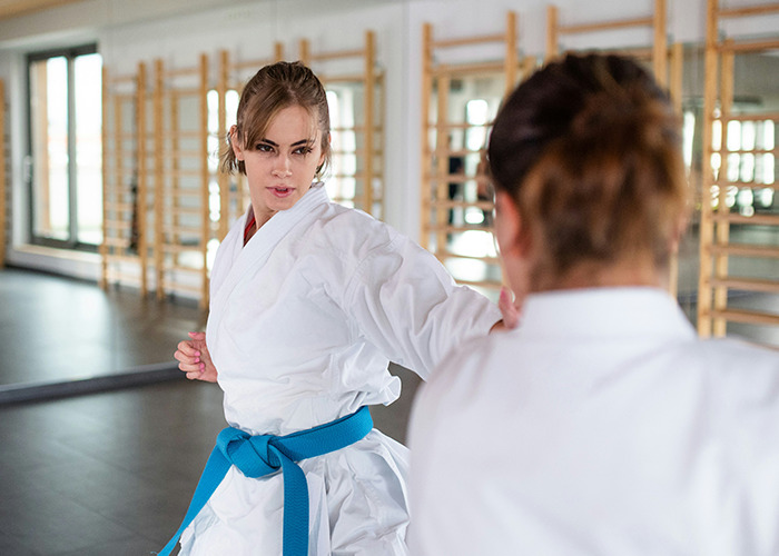 Two women practicing martial arts in a gym, wearing white uniforms, focused on a training session.