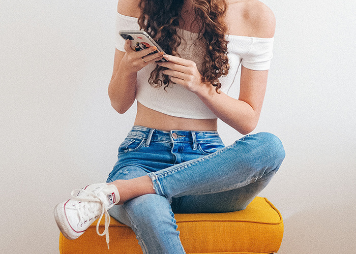 Young woman in casual attire using phone, sitting on a yellow chair, potentially exploring diet tips or trends.