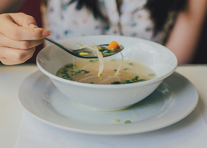 A person eating a bowl of broth with vegetables, representing a diet.