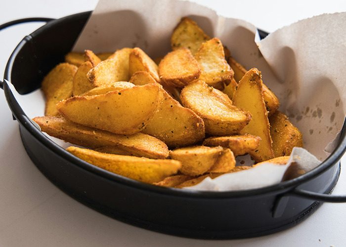 Potato wedges in a black dish on parchment, illustrating unhealthy diet choices.