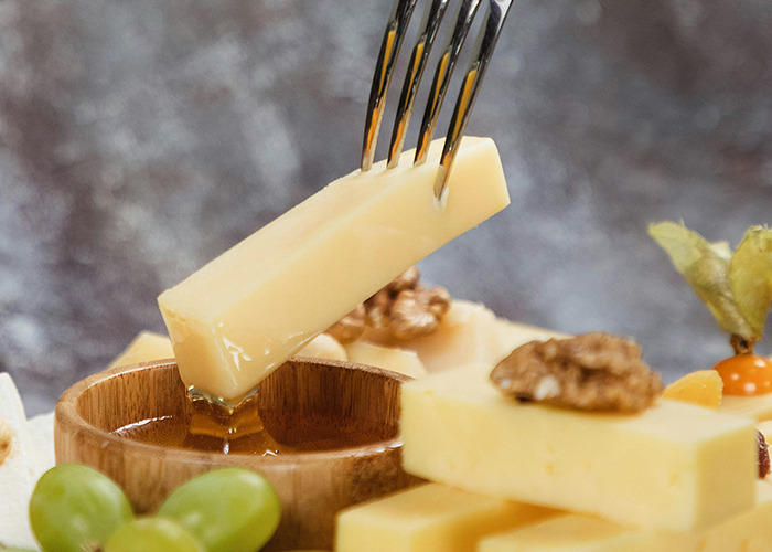 Fork dipping cheese into honey, surrounded by grapes and walnuts, illustrating unusual diet choices.