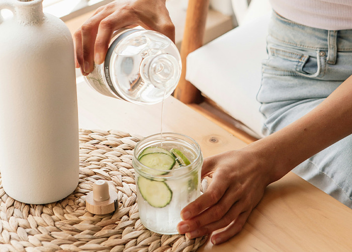 Pouring water into a jar with cucumber slices on a wooden table, highlighting a healthy diet choice.