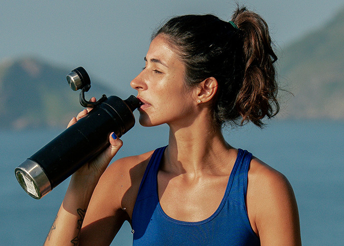 Woman in a blue tank top drinking water outdoors, symbolizing the complexity of diets.