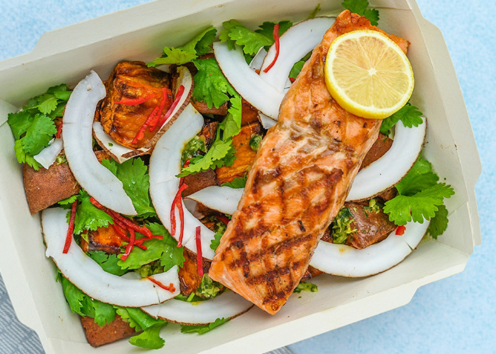 A healthy meal with grilled salmon, coconut slices, and fresh greens.