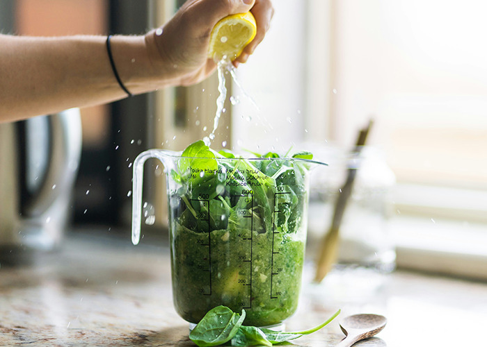 Squeezing lemon over spinach in a measuring cup, representing extreme diet choices.