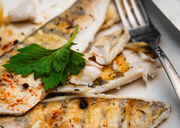 Grilled fish with herbs and spices, illustrating a diet example on a white plate with a fork.