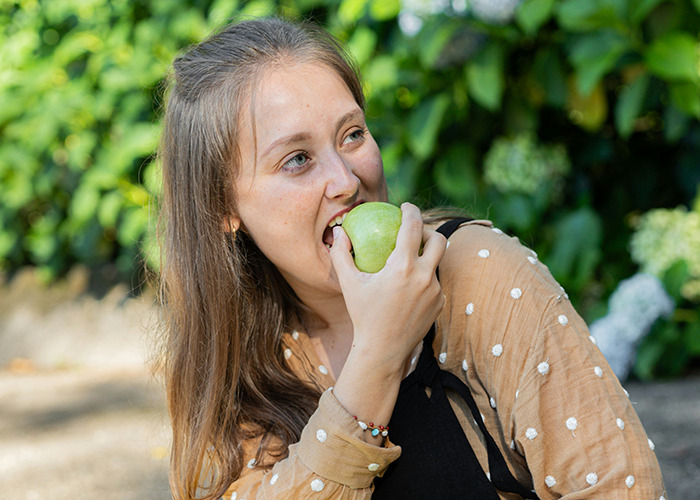 Person eating a green apple, symbolizing diet choices, with greenery in the background.
