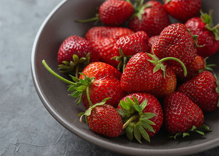 A bowl of fresh strawberries on a dark surface, related to worst diets.