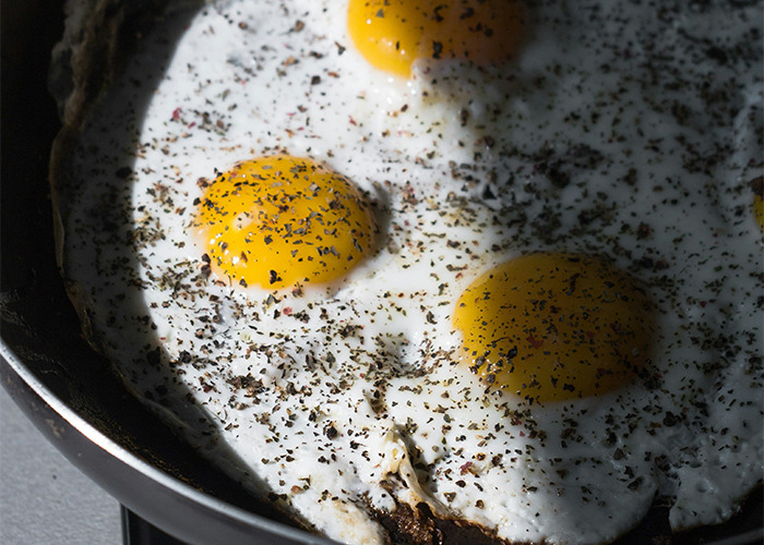 Three sunny-side-up eggs with herbs on a skillet, highlighting a diet meal.