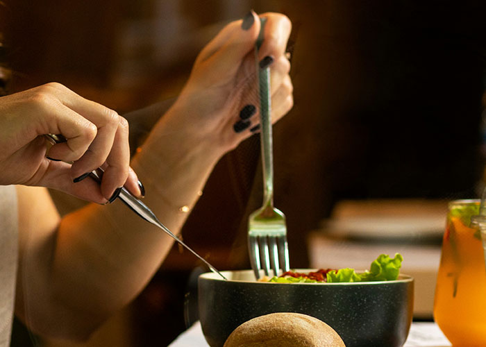 Person dining with salad, using fork and knife, highlighting diet choices.