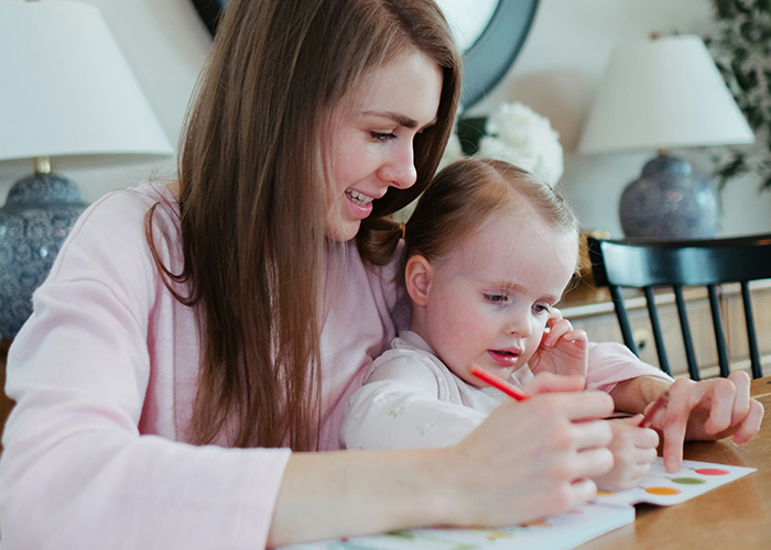 Woman practicing gentle parenting, guiding a toddler with coloring, sitting in a cozy home setting.