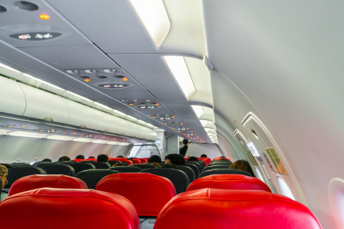 Passengers seated inside an airplane cabin, viewed from the rear, with red and black seats, suggesting in-flight drama.