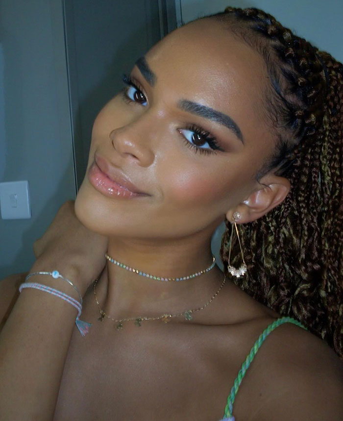 Transgender actor with braided hair, wearing delicate jewelry, smiling warmly in a close-up photo.