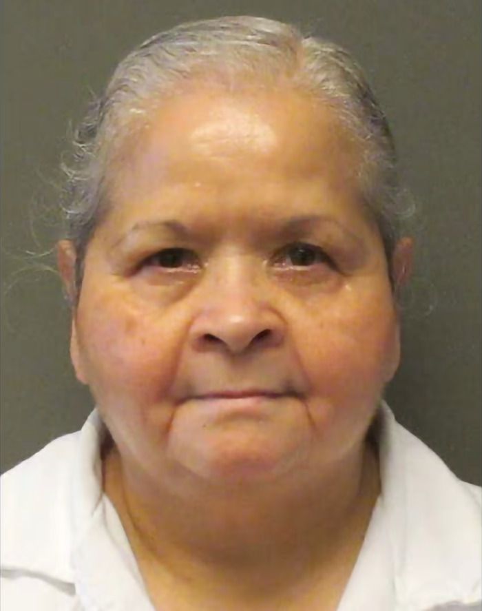 Woman involved in pop star Selena's assassination, in prison attire, against a gray backdrop.