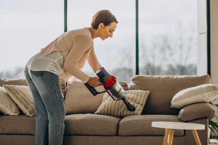 Person using a cordless vacuum on a sofa. Revolutionary life-changing product under $500.