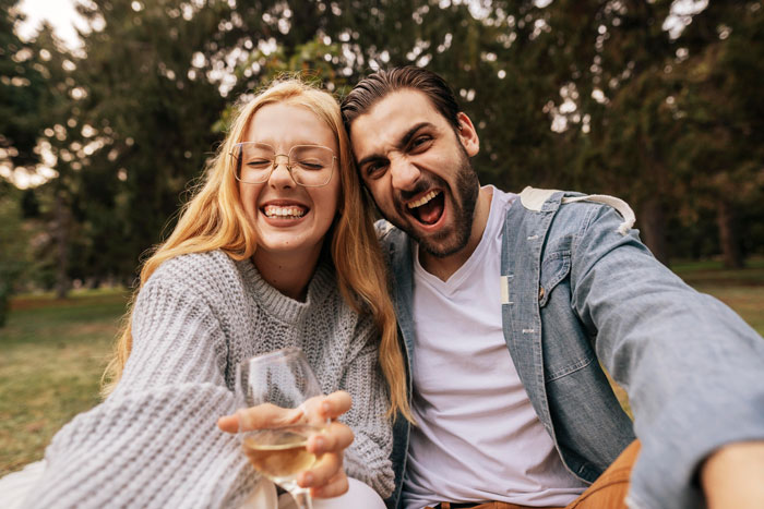 Woman with man's crush, both smiling outdoors, holding a glass, enjoying a sunny day.