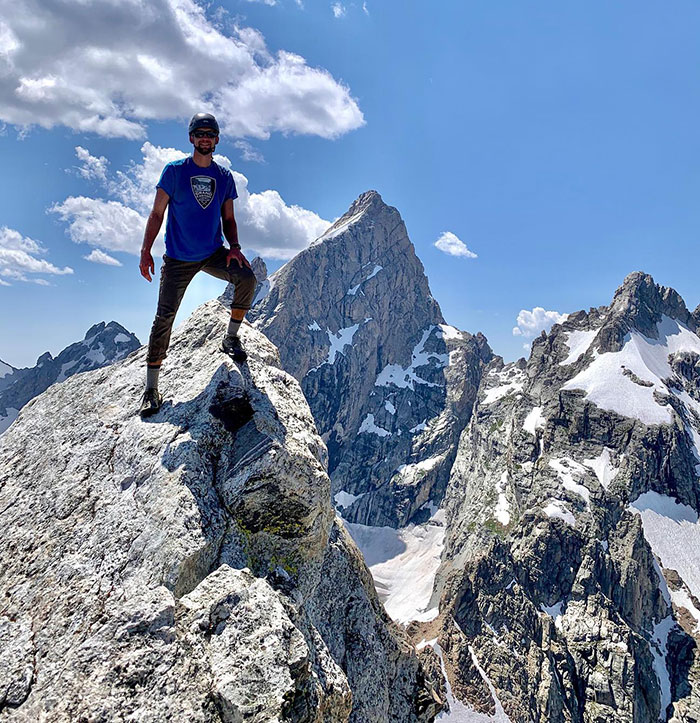 Man standing on mountain peak with snow and rocky terrain, under clear sky. Man standing on mountain peak with snow and rocky terrain, under clear sky.