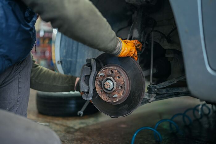 Mechanic working on a car brake system, wearing orange gloves, illustrating "mess around find out" in automotive repair.