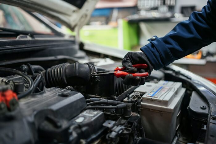 Mechanic repairing car engine with pliers, wearing gloves, during a challenging job interview scenario.
